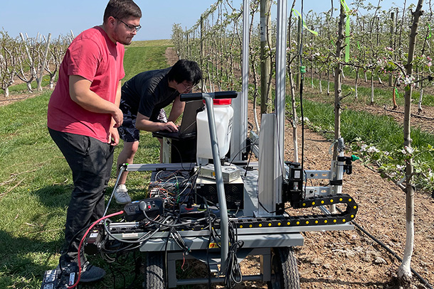 two individuals in an orchard operating equipment