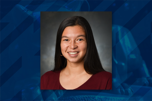 A formal headshot of an individual on a blue background.