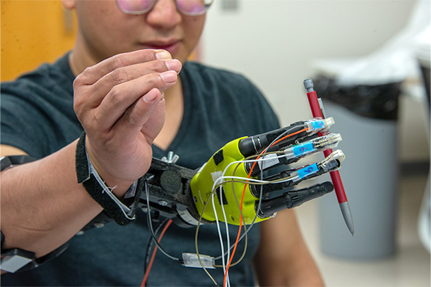 A person demonstrates how to use a prosthetic hand to lift a pencil.