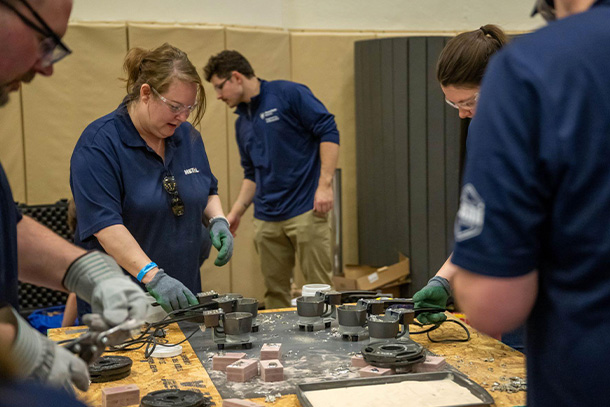 image of several individuals, all in blue shirts, working over a table of metal parts