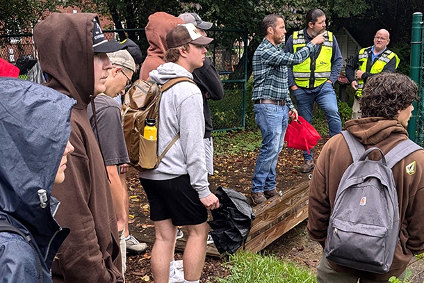 a group of individuals with jackets and backpacks stand in the woods