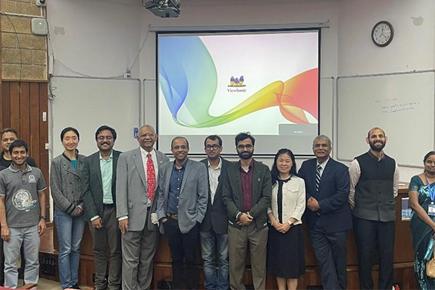 a small standing group of people smile for photo in front of projector screen