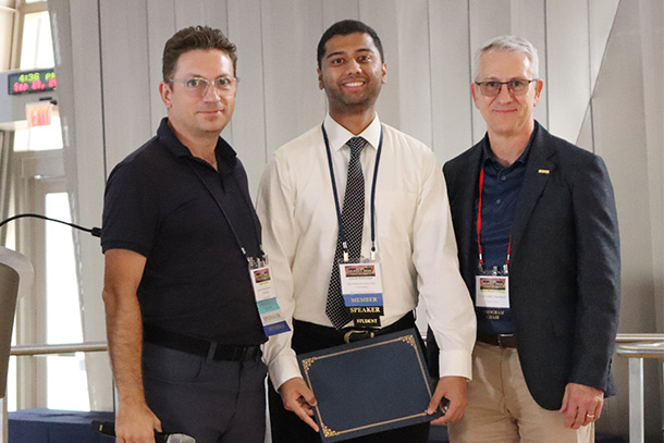 3 people standing in a row, one receiving an award at a conference.