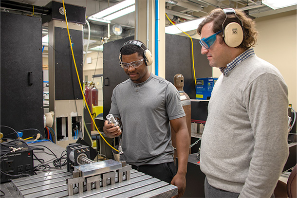 Two individuals look down at a ultrasonic lab setup in a lab setting. 