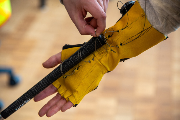 A golf club attaches to a yellow glove via a thin wire that holds it in place.