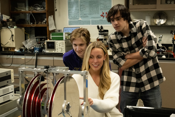 Three students lean over lab equipment.