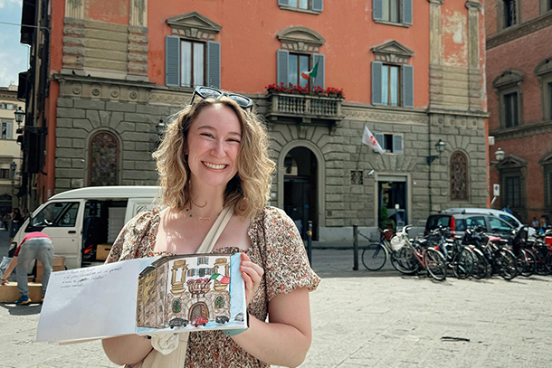 An individual holds an open book in fromt of a building.