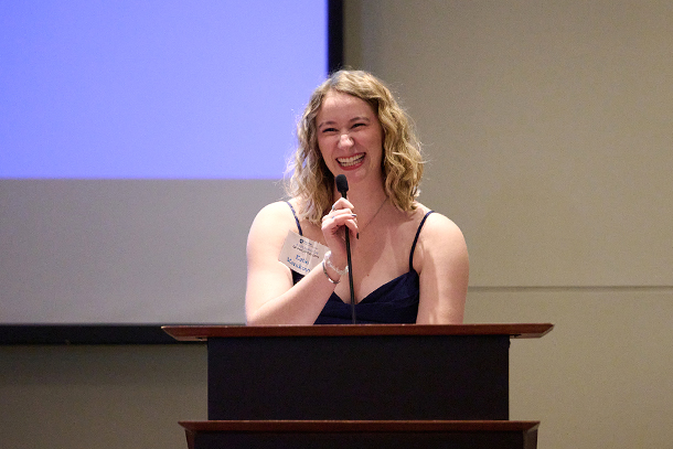 an individual speaks at a podium in front of a screen.