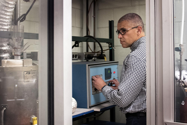 Person stands looking off camera while turning dial on a piece of machinery