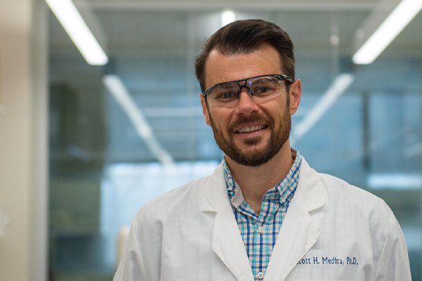 A portrait of a person in a white lab coat and a pair of safety glasses