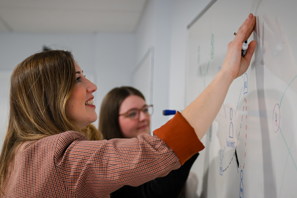 Two individuals draw on a whiteboard.