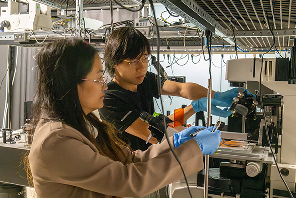 Two individuals manipulate lab equipment in a lab.