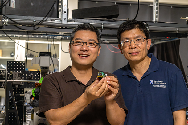 Two individuals pose in a lab holding a small device known as a metasurface. 