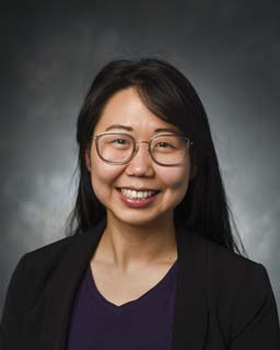 Headshot of a person in glasses, a purple blouse, and a suit jacket