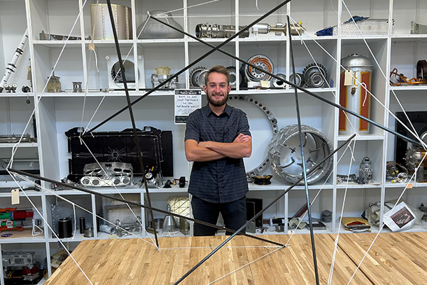 A person poses with arms crossed behind a structure on a table. 