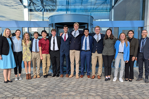 Students and faculty members in business professional attire pose in a line for a photo outside the Pratt & Whitney Customer Training Center. 