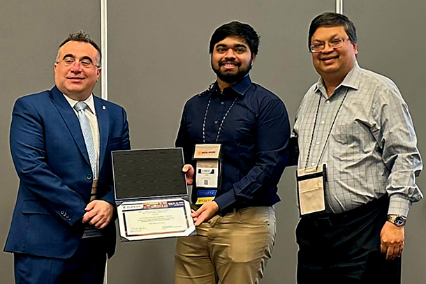 Three individuals, one holding an award, pose for a photo. 