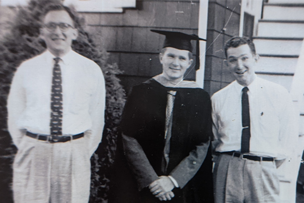 A black-and-white photo of three brothers, one wearing a cap and gown, posing outdoors.