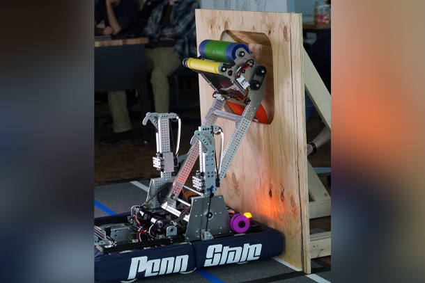 A robot places a foam ring in a slot in a wooden board. class=