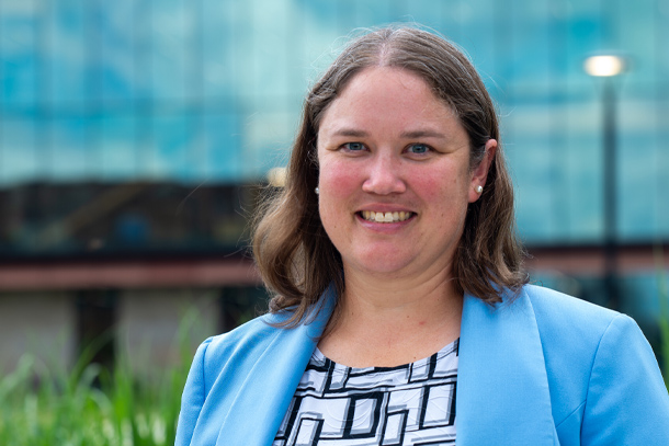 A portrait of a person in a blue blazer smiling at the camera outside. 