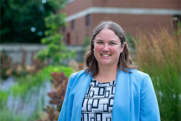 Woman standing in front of bush, professional headshot in front of a building.