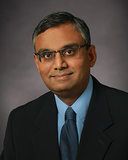 Headshot of a person in glasses, a suit, and a tie. 