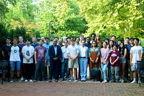 A large group of electrical engineering students and faculty pose outdoors on a brick walkway 