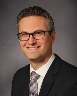 headshot of a person in a suit and tie and glasses 