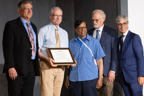 An individual receives an award plaque surrounded by four others.  