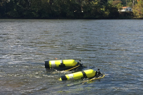 Two swimmers using scuba gear swim at the surface of a river.