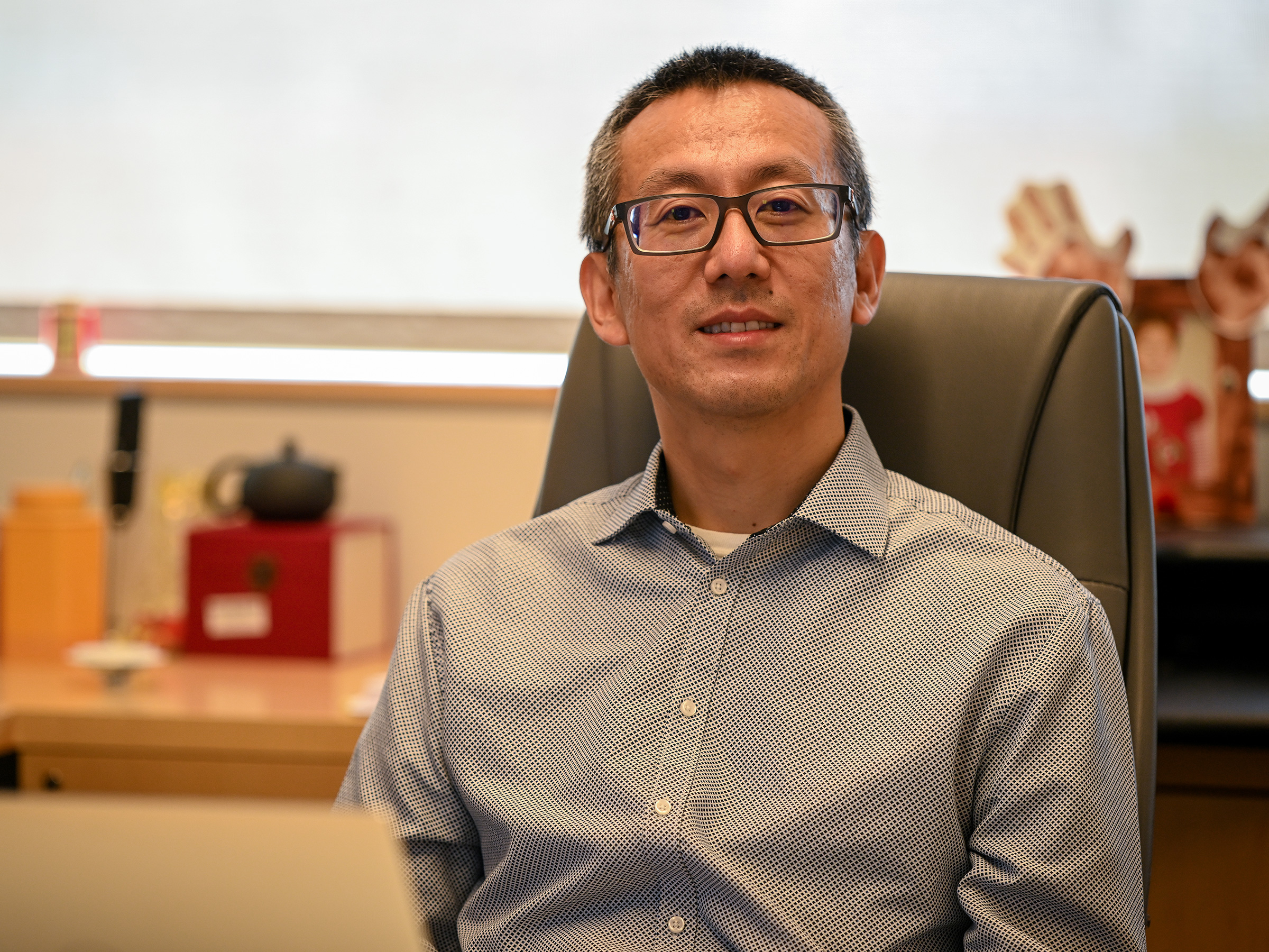 A person in glasses sits at a desk chair.