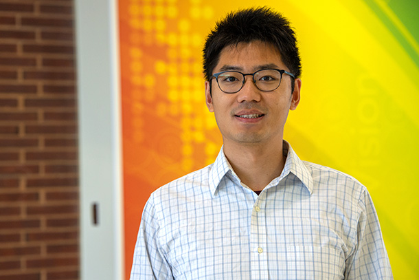 A portrait of an individual standing behind a brick, orange, green and yellow backdrop. 