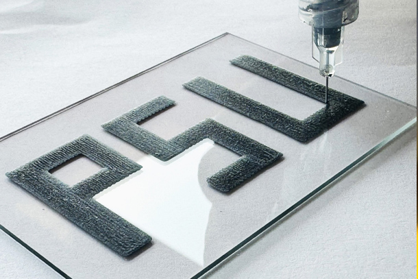 A 3D-printing device is held over a recently printed sample that says PSU. 