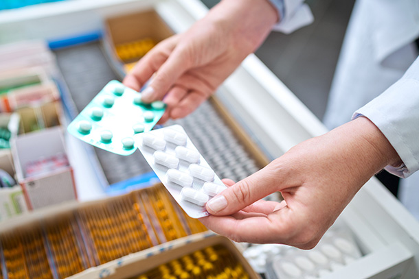 Two packs of pills being held above a drawer containing more pharmaceuticals.