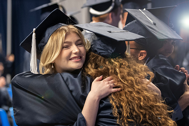two individuals dressed in cap and gown in an embrace