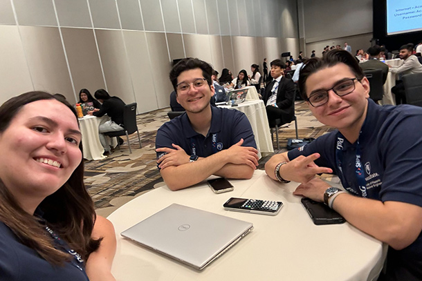 Three students pose around a table at a conference.