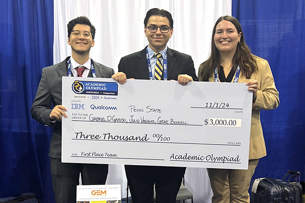 Three individuals hold a large check at a conference booth.