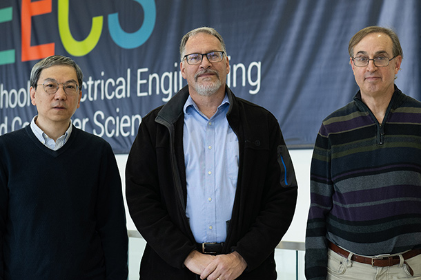 Three people pose outside in front of an electrical engineering and computer science banner.