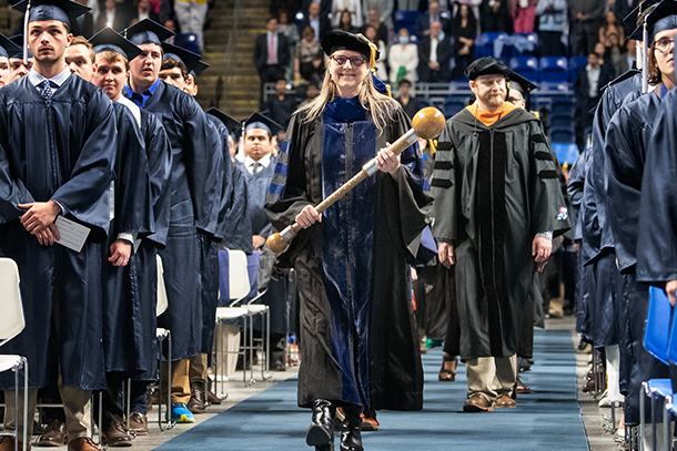 Person walking down aisle at commencement, surrounded by others watching on.