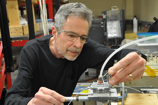 Person with gray hair and glasses touches metal box.