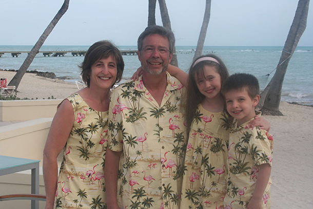 A family portrait of two adults and two kids posing at a beachfront.