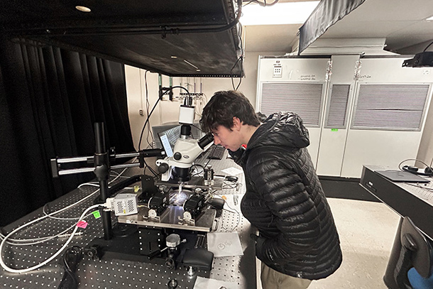 Person standing in a lab looking through a microscope at a machine