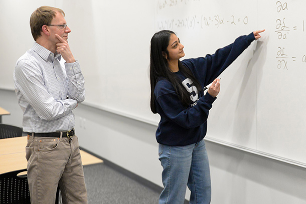 Two individuals examine a math problem on a whiteboard