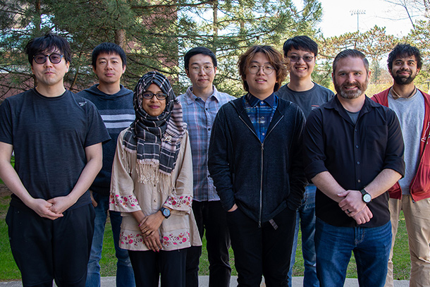Eight people stand in a line to pose for a photo outdoors.