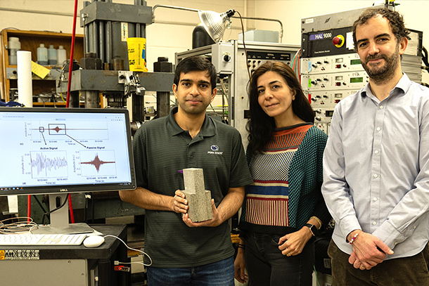 Three people pose in a lab next to a computer screen. One person holds two granite blocks.