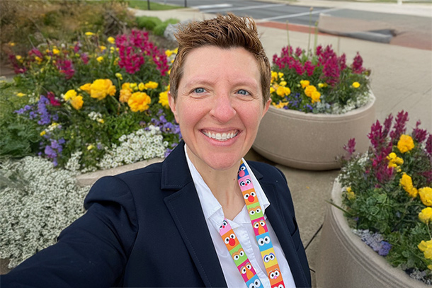 A person looks at the camera smiling standing in front of flowers.