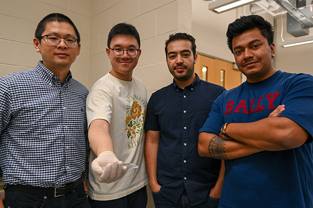 Four people pose for a photo with the second person holding a sample on a sample box.