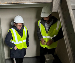 Two people wearing hard hats and safety vests stand in a stairwell