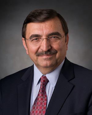 A professor wearing glasses and a suit and tie poses for a professional headshot.