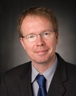 A headshot of a professor wearing glasses and a tie.